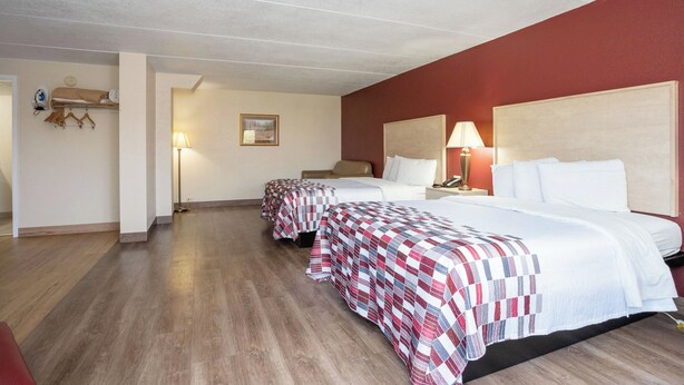 A hotel room with two beds, wooden flooring, and a red accent wall.