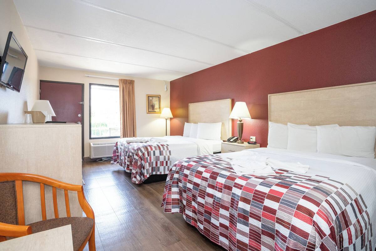 A hotel room with two beds, a desk, a chair, a TV, and a window with curtains.