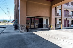 Entrada de un hotel con fachada de piedra, puertas de vidrio y un estacionamiento al frente.