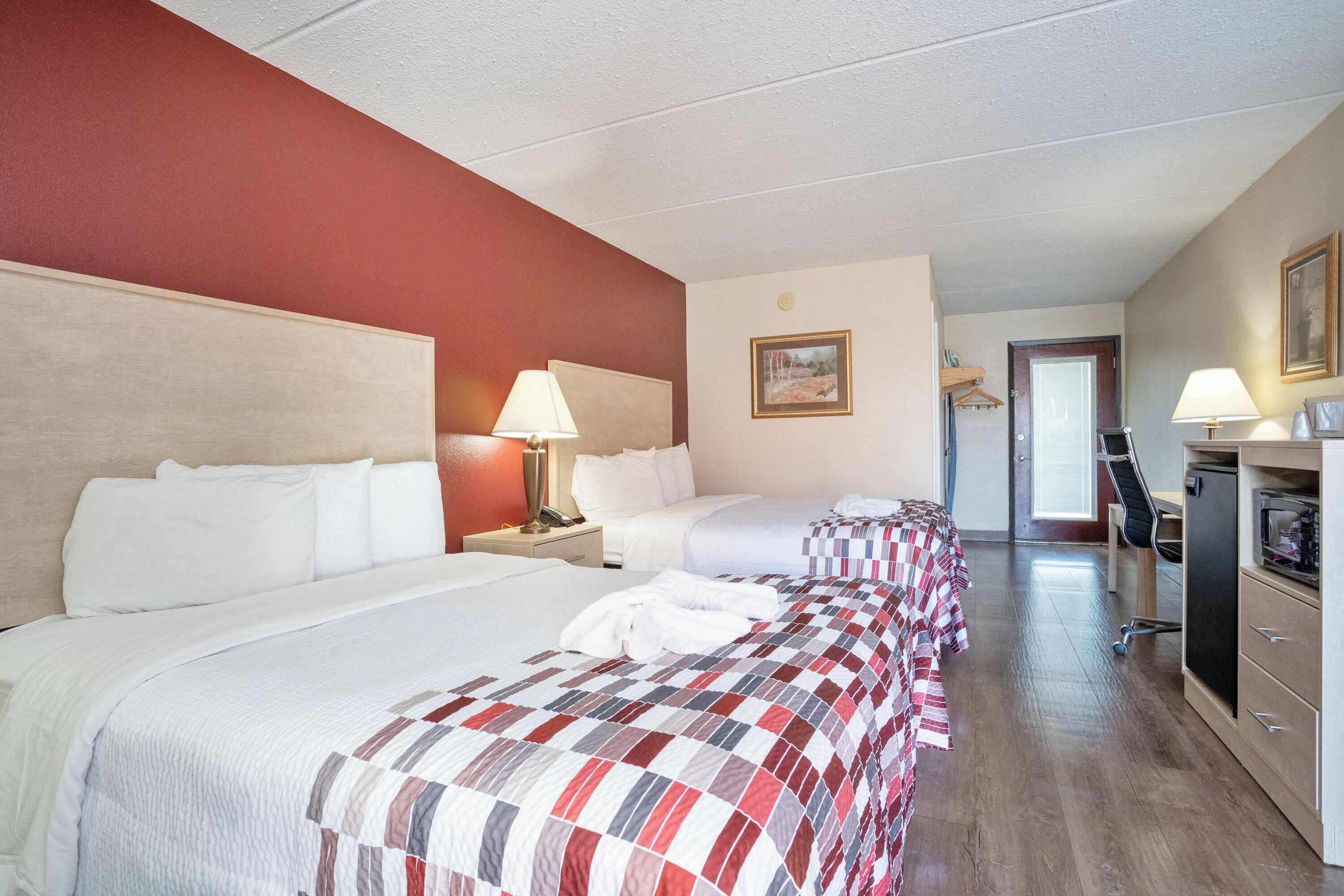 A hotel room with two beds, a desk, a chair, and a door leading to a bathroom.