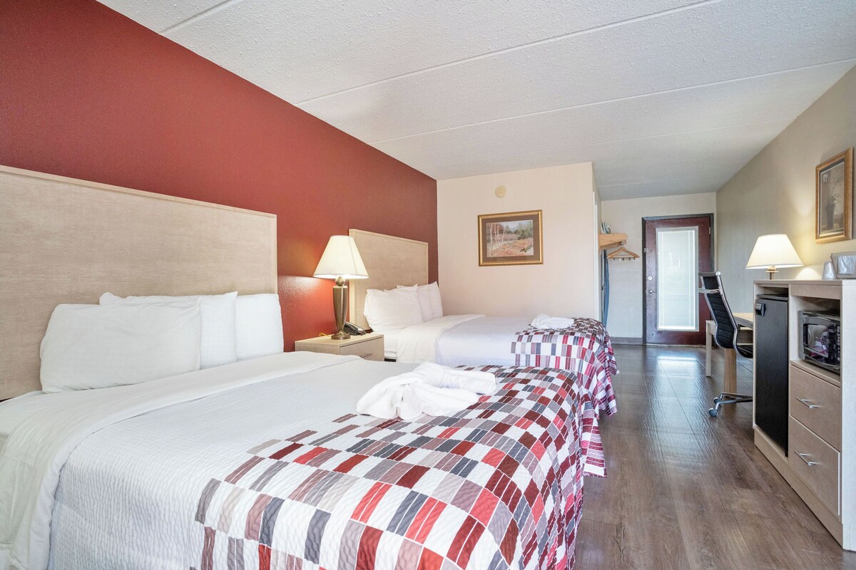 Una habitación de hotel con dos camas, un escritorio, una silla y una puerta que da a un baño.