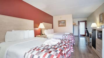 A hotel room with two beds, a desk, a chair, and a door leading to a bathroom.