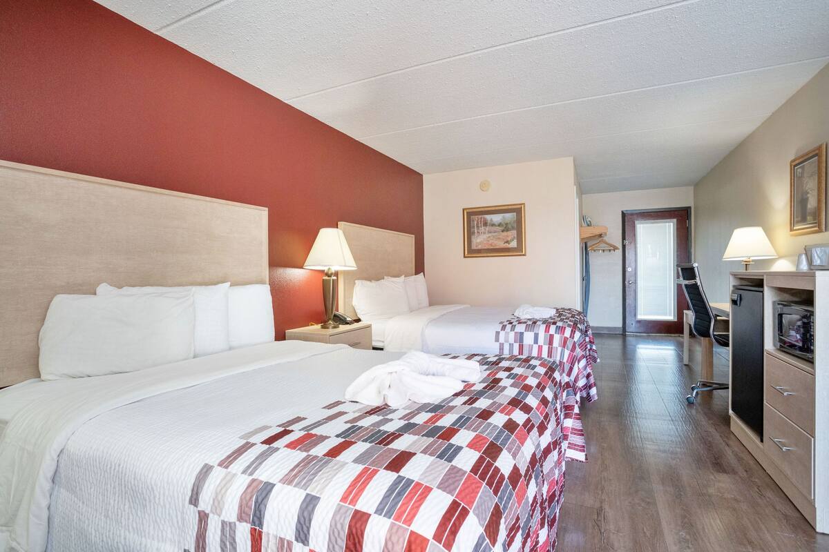A hotel room with two beds, a desk, a chair, a TV, and a door leading to the hallway.