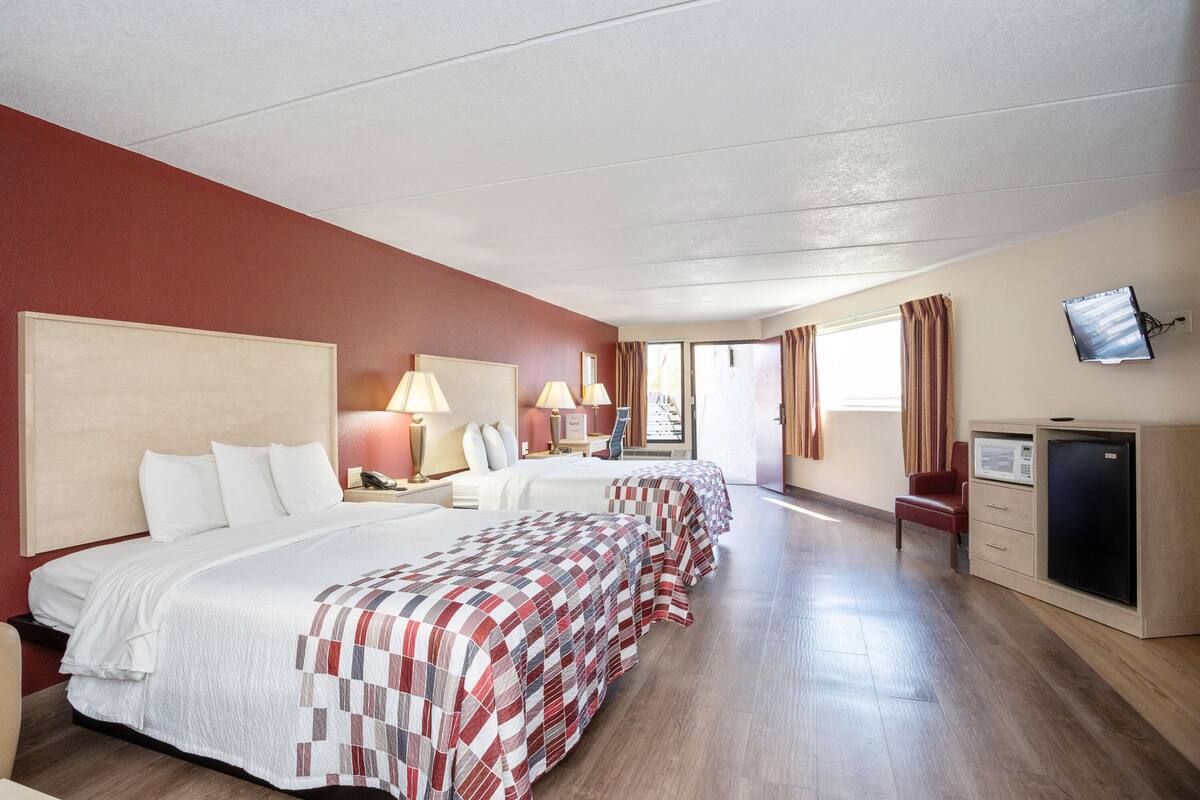 A hotel room with two beds, a desk, a chair, a television, and a microwave.
