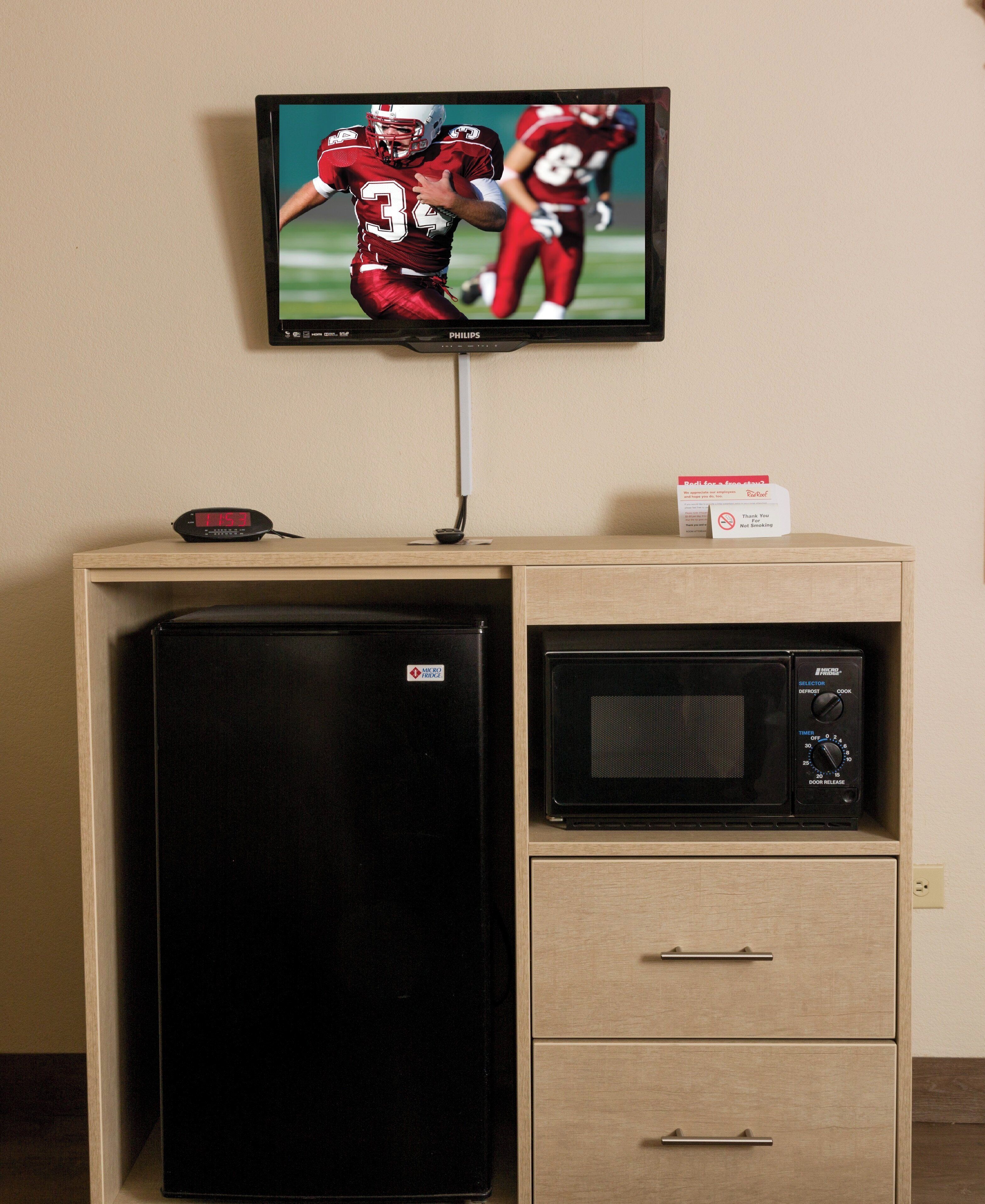 A kitchenette with a refrigerator, microwave, and a television mounted on the wall.