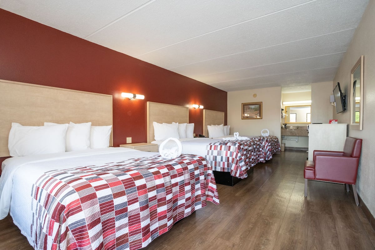 A hotel room with three beds, a red chair, and a kitchenette.