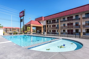 Un hotel con piscina, zona cubierta y edificio de techo rojo.