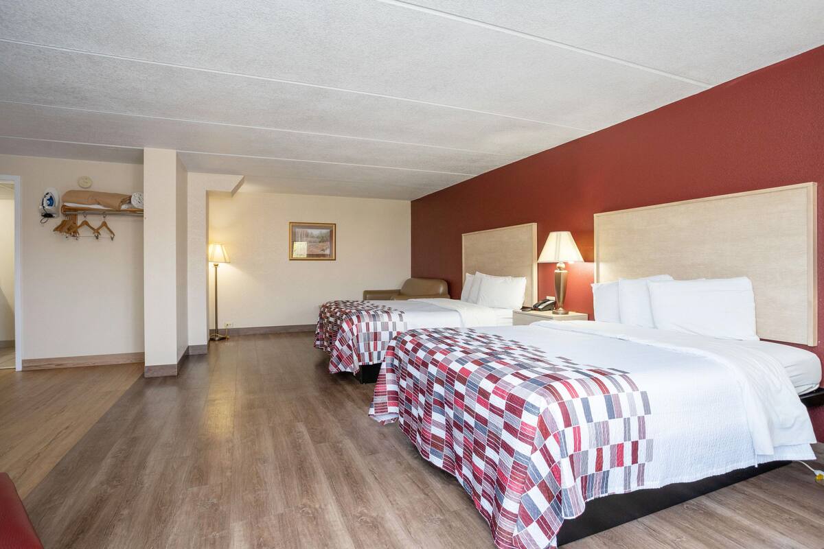 A hotel room with two beds, wooden flooring, and a red accent wall.