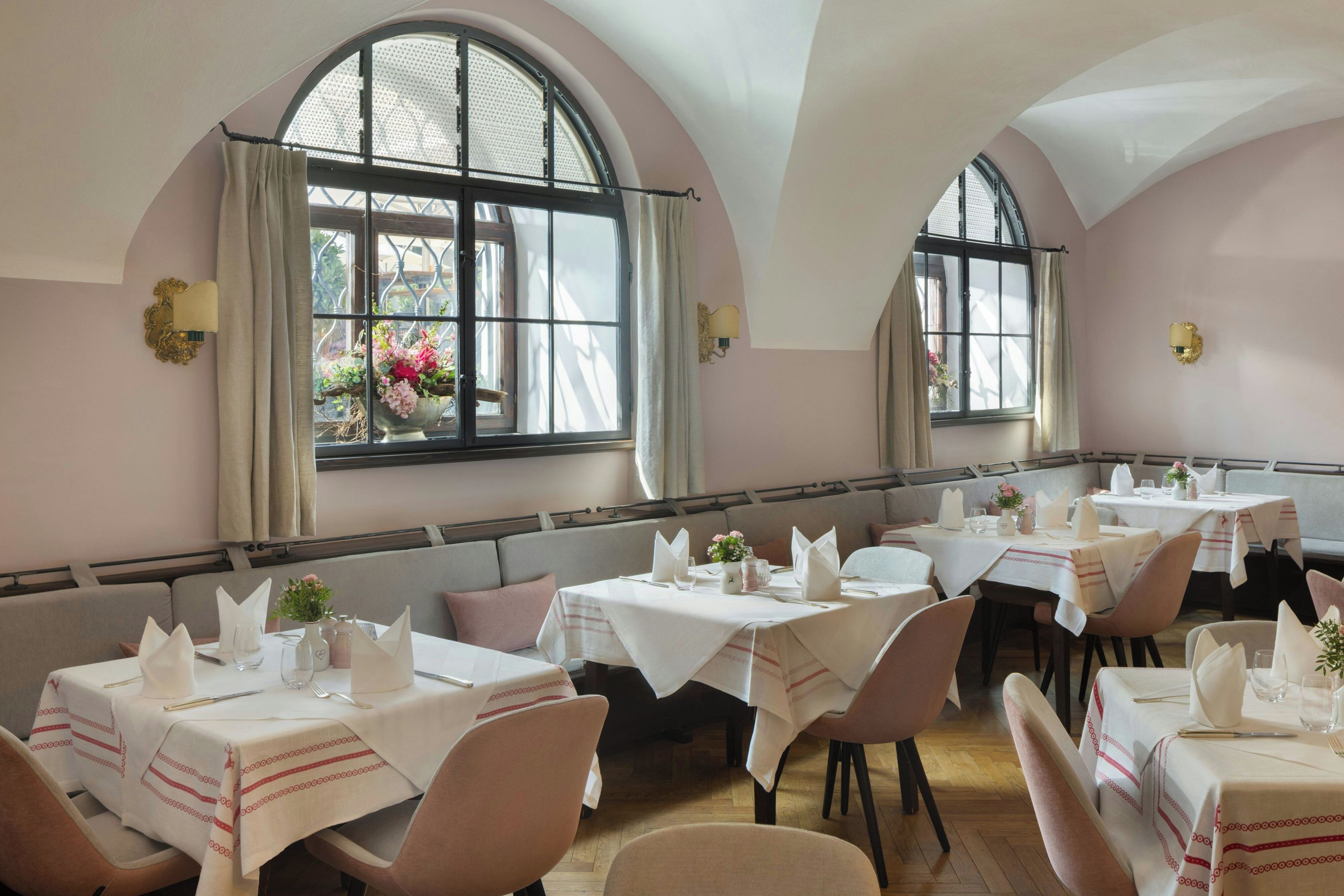 Un comedor con mesas dispuestas para el servicio, amplias ventanas arqueadas y vistas al exterior.