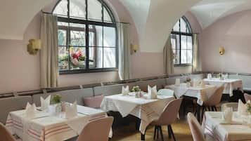 Un comedor con mesas dispuestas para el servicio, amplias ventanas arqueadas y vistas al exterior.