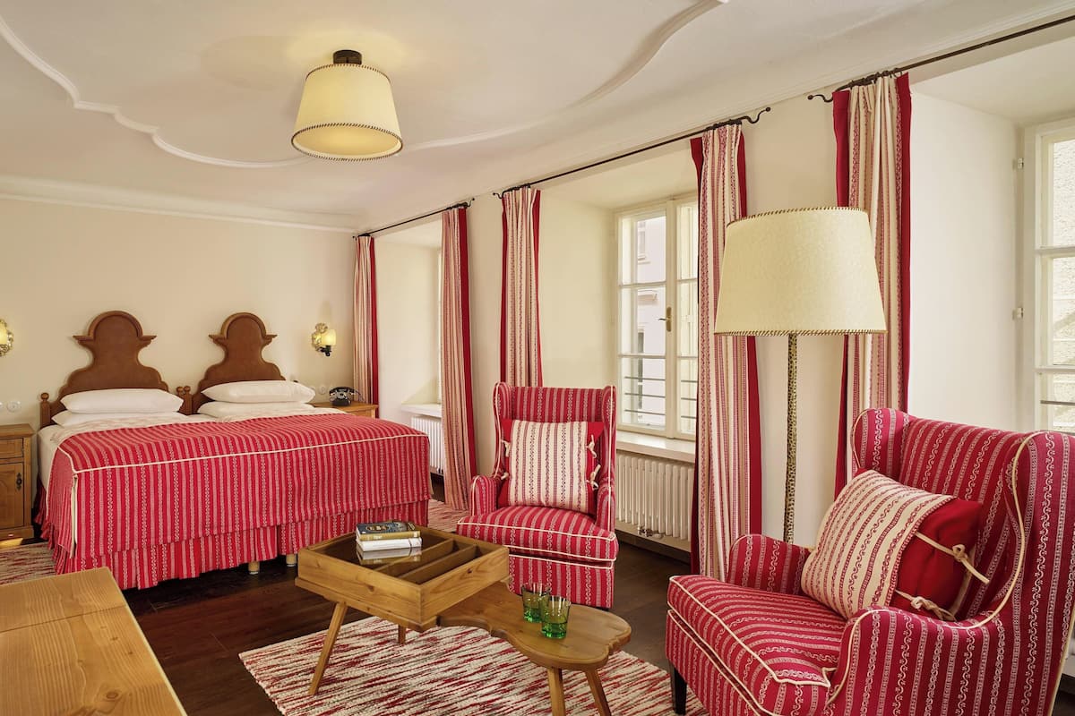 A hotel room with two beds, a red-striped armchair, a wooden coffee table, and a lamp.