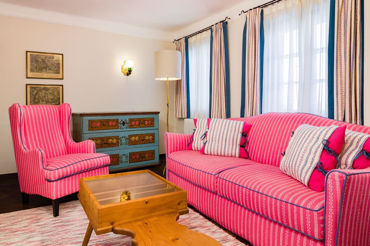 A living room with a pink-striped sofa, a matching armchair, a wooden coffee table, and a blue cabinet with floral patterns.