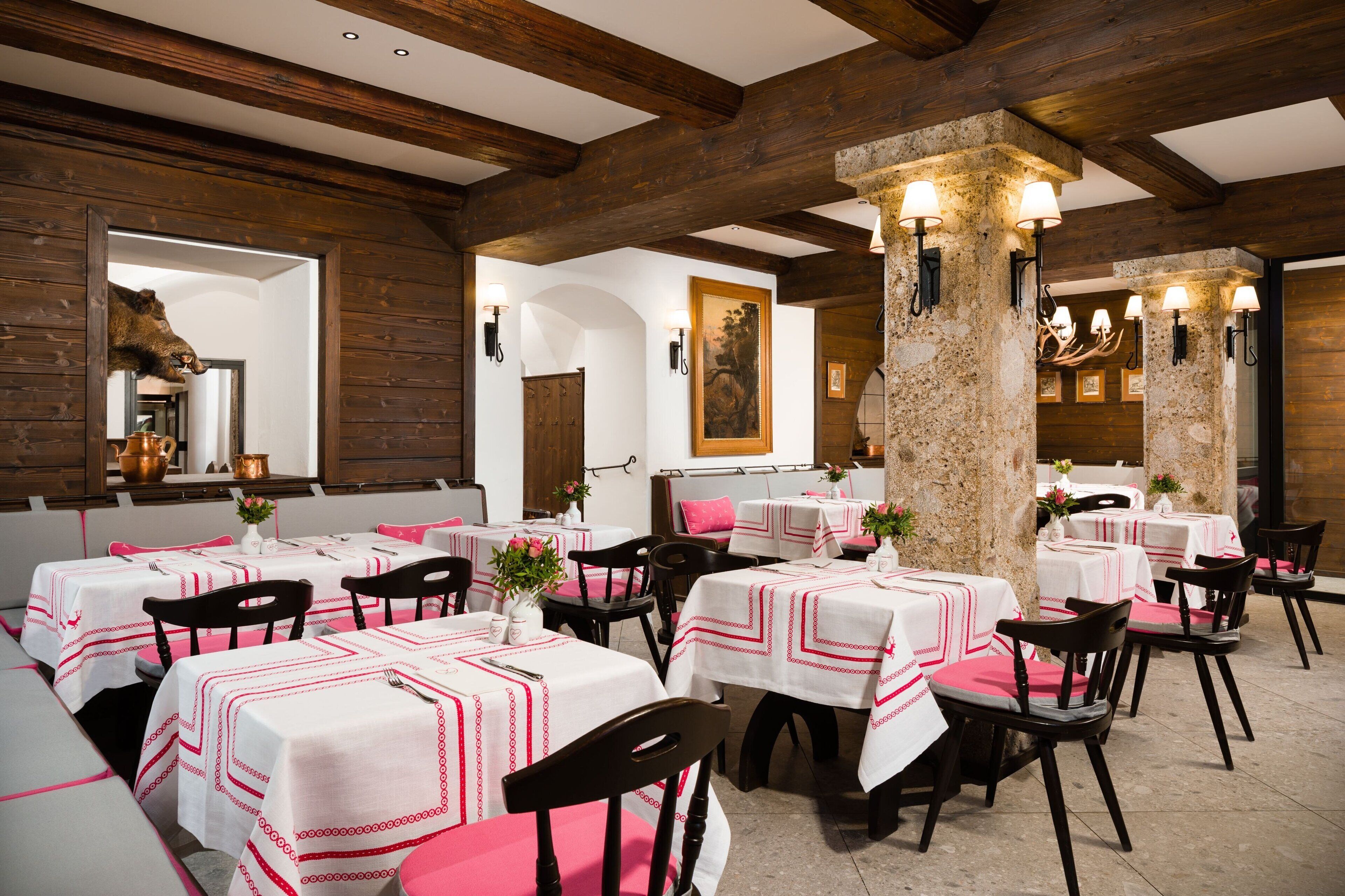 A restaurant with multiple tables and chairs, wooden beams on the ceiling, and stone pillars.