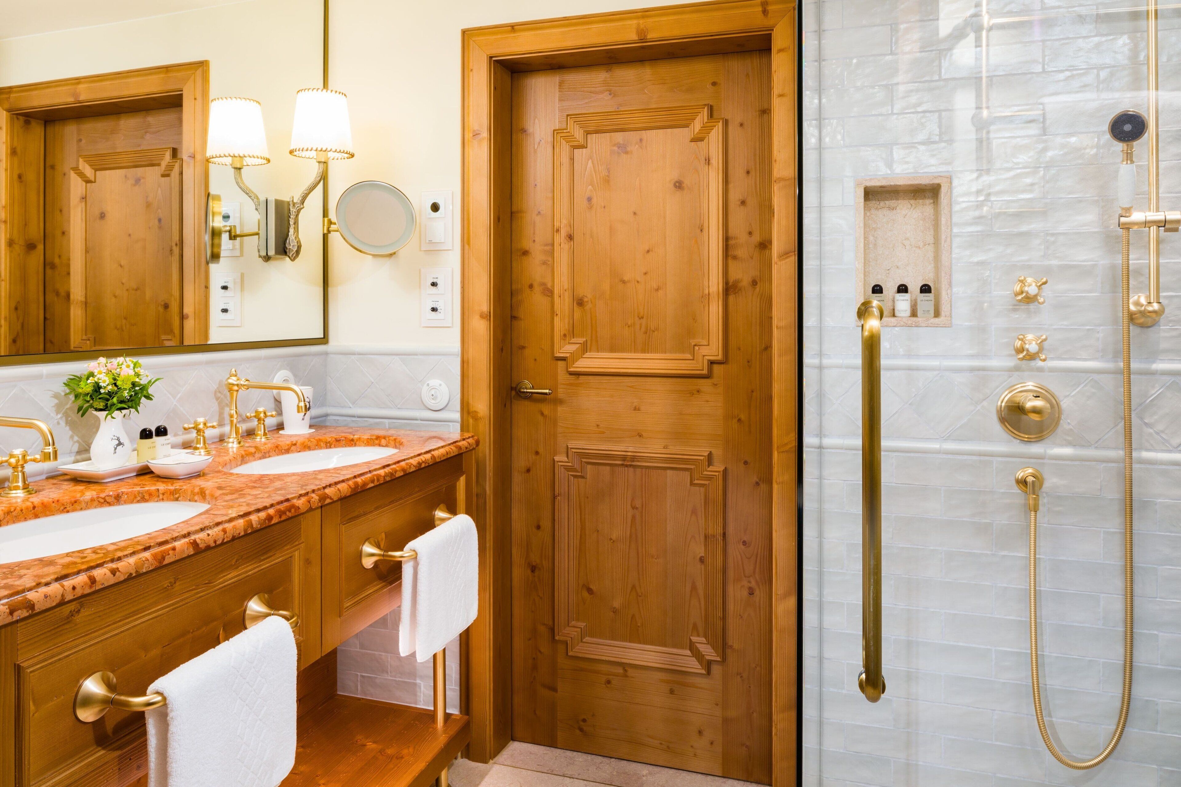 Ein Badezimmer mit zwei Waschbecken, einer Holztür und einer Dusche mit goldfarbenen Armaturen.