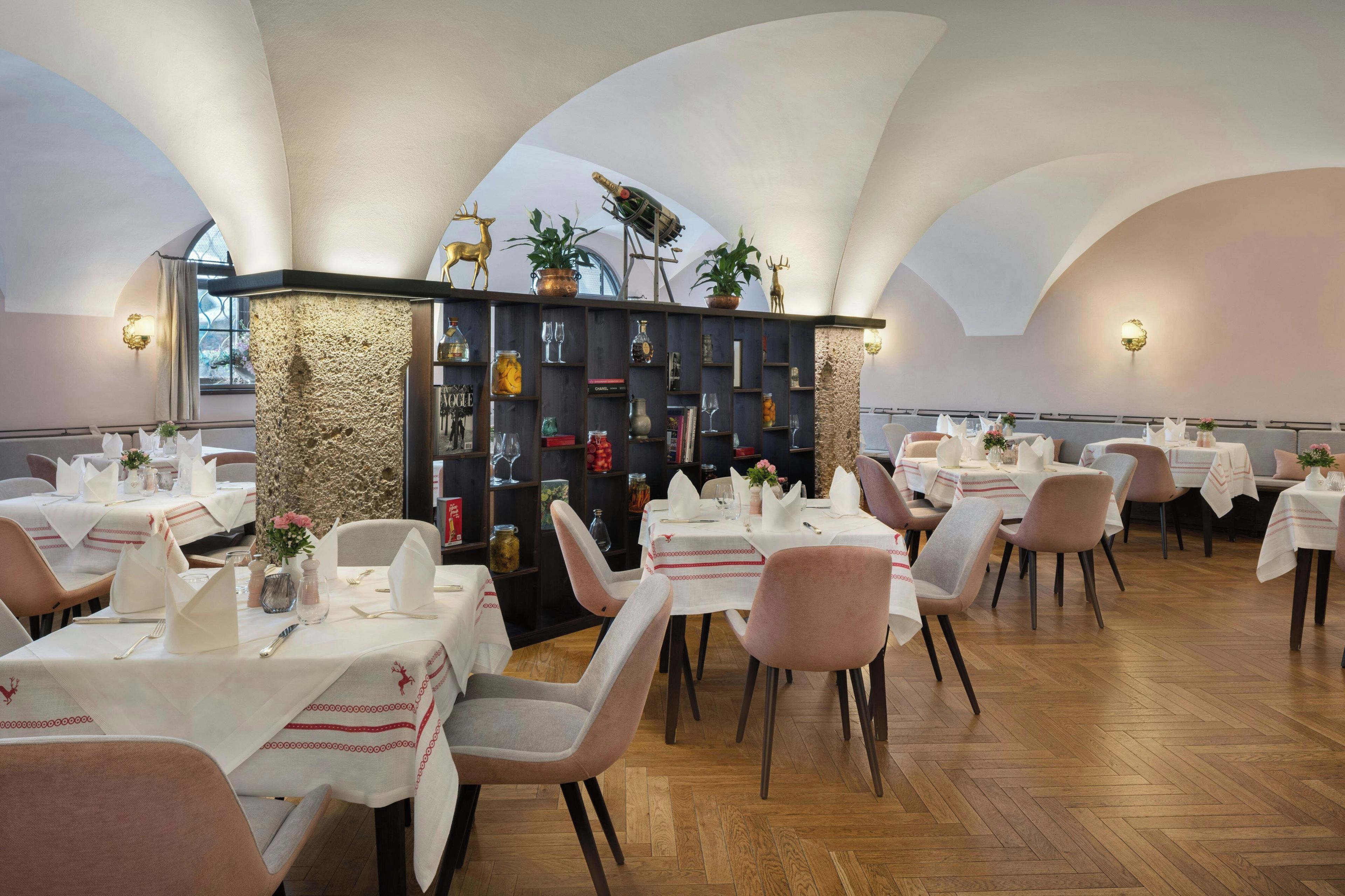 Een restaurant met meerdere tafels, stoelen en een decoratieve boekenkast in het midden.
