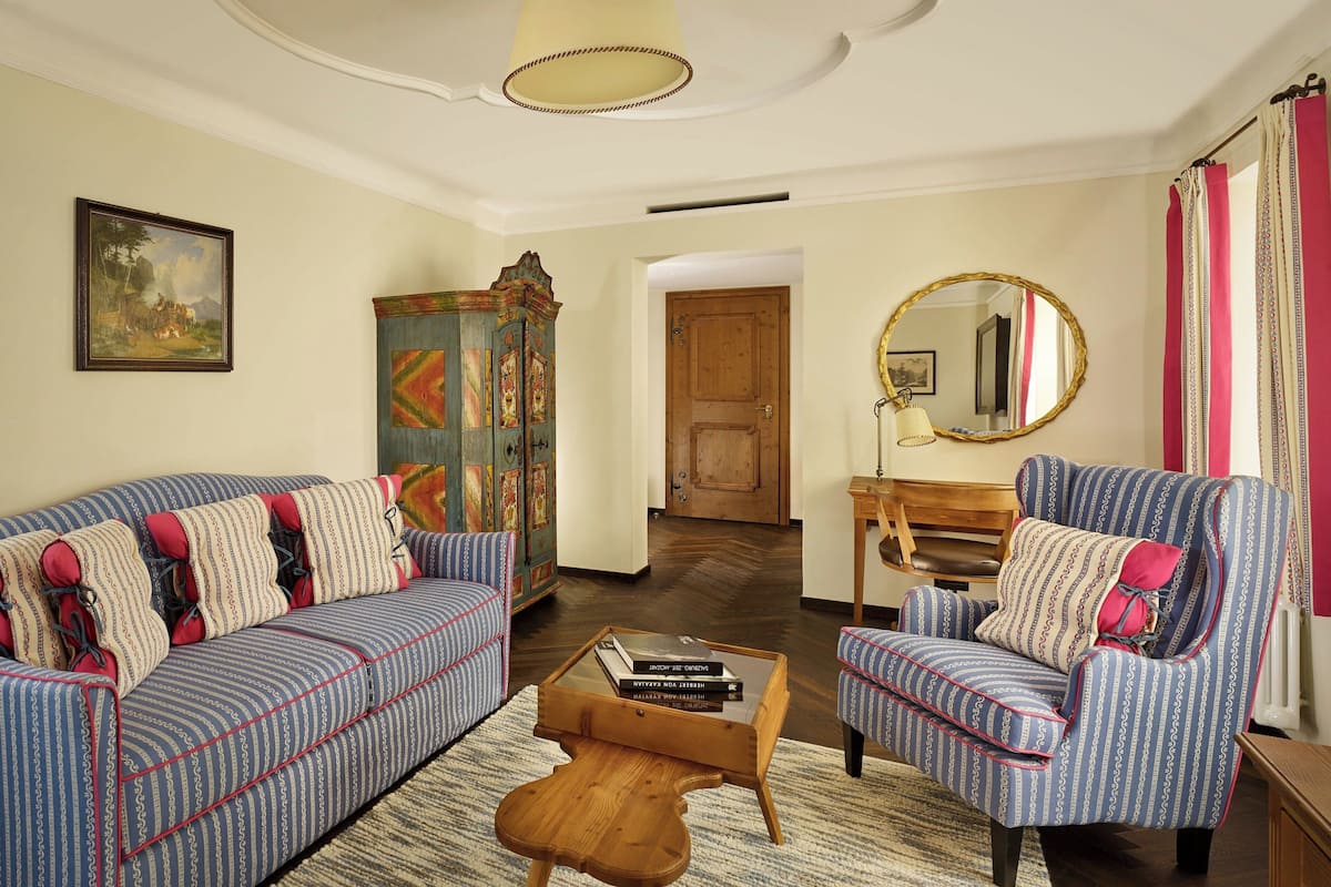 A living room with a blue-striped sofa, a patterned armchair, a wooden coffee table, and a colorful cabinet.