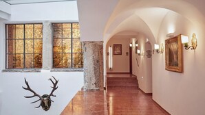 A hallway with a stone column, a mounted deer head, and a staircase leading to another level.