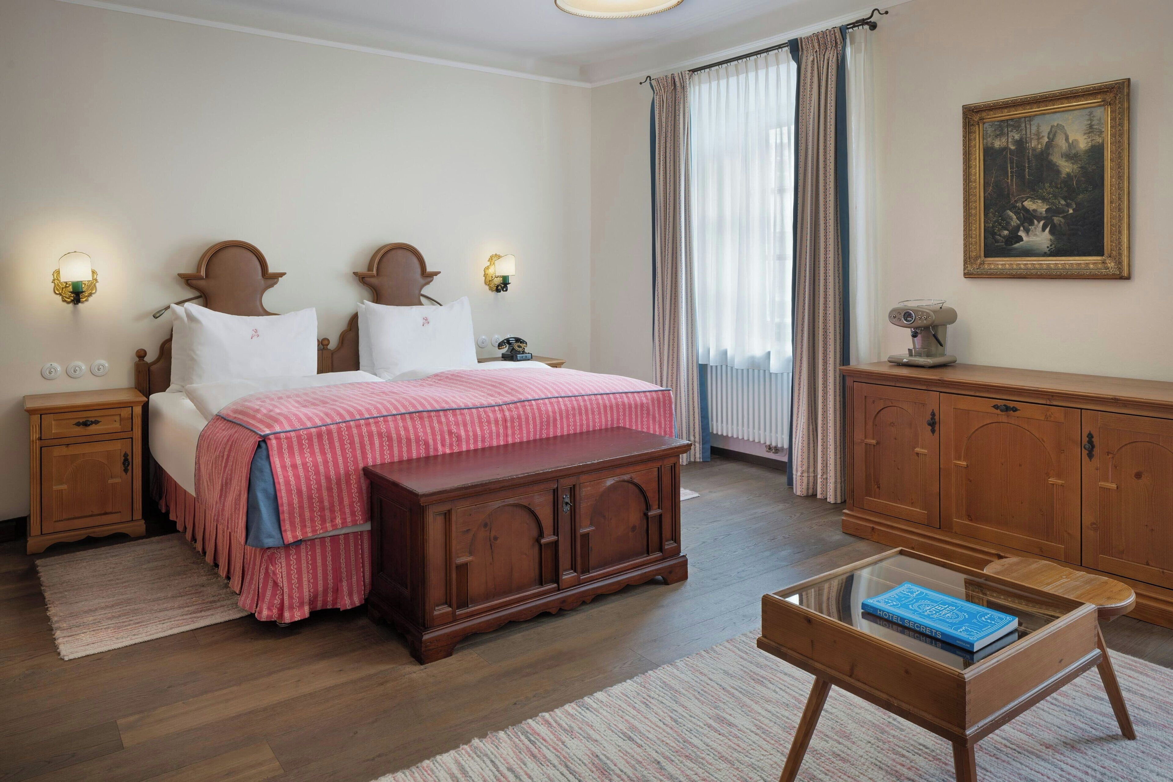 Une chambre avec un lit double, des tables de chevet en bois, une commode, une table basse en verre avec un livre dessus et un tableau au mur.