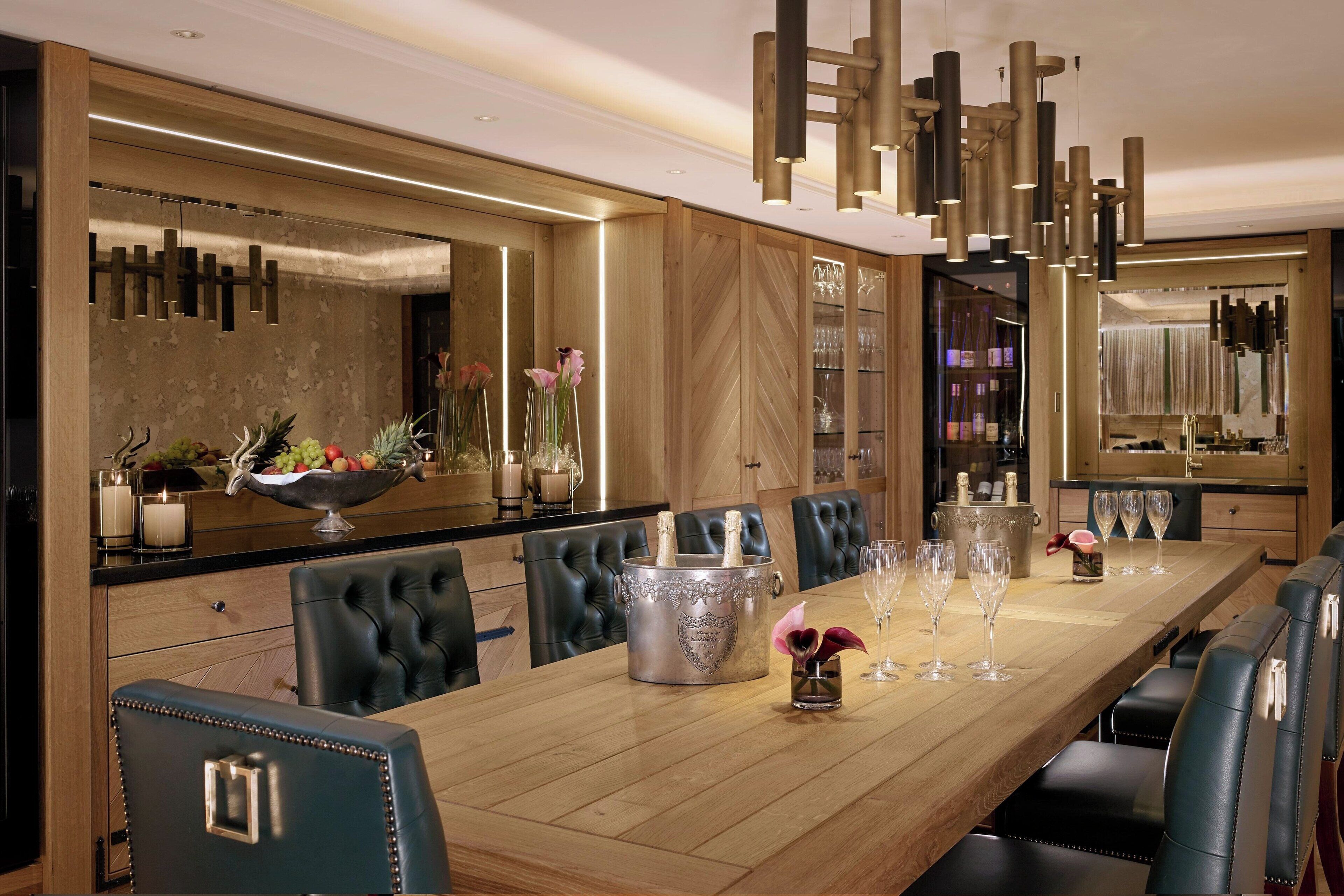 A long dining table with a champagne bucket, wine glasses, and flowers. There are leather chairs around the table.