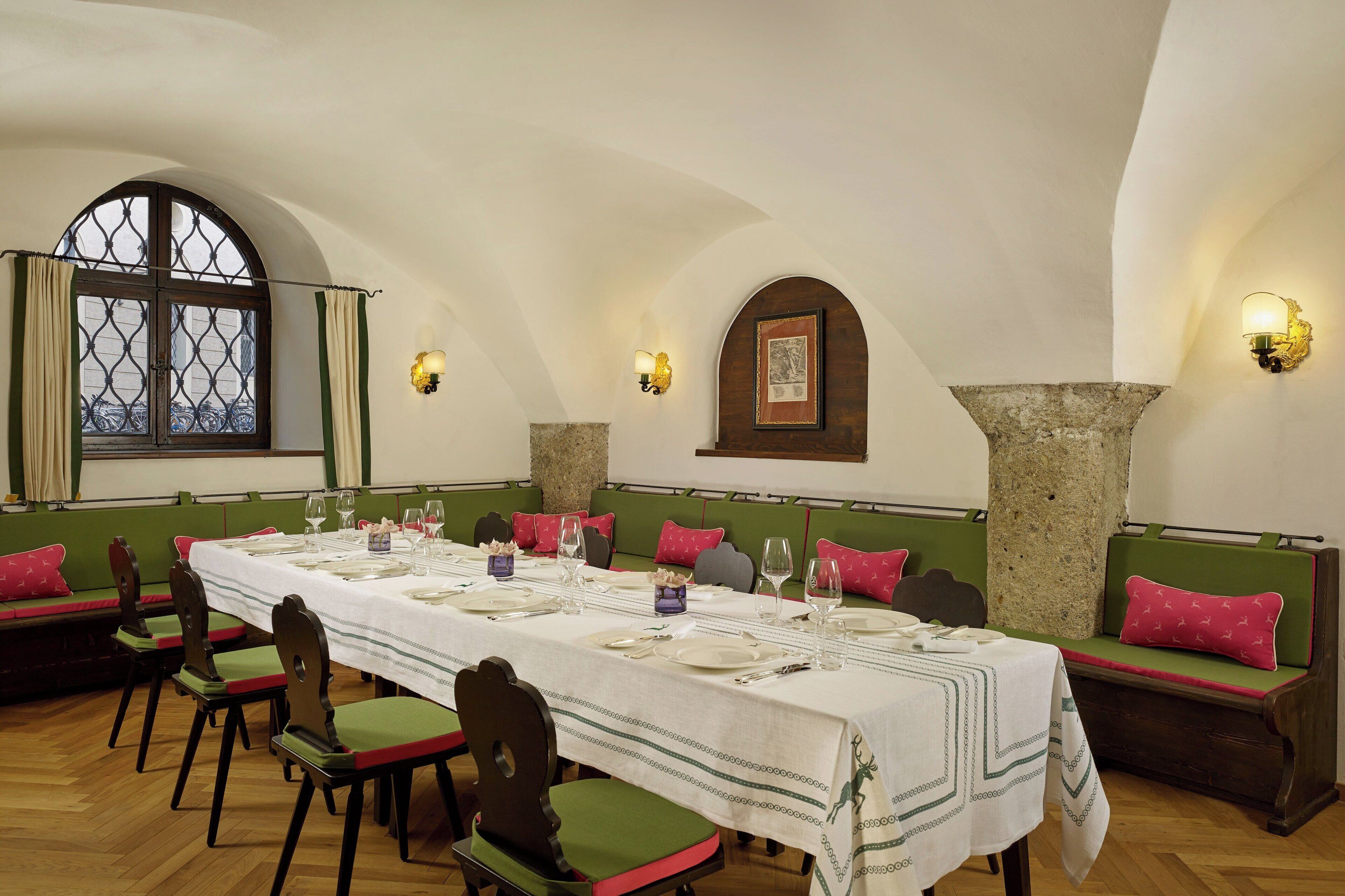 A dining area with a long table set for a meal, green cushioned benches, and stone pillars.