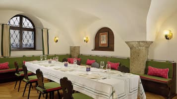 A dining area with a long table set for a meal, green cushioned benches, and stone pillars.