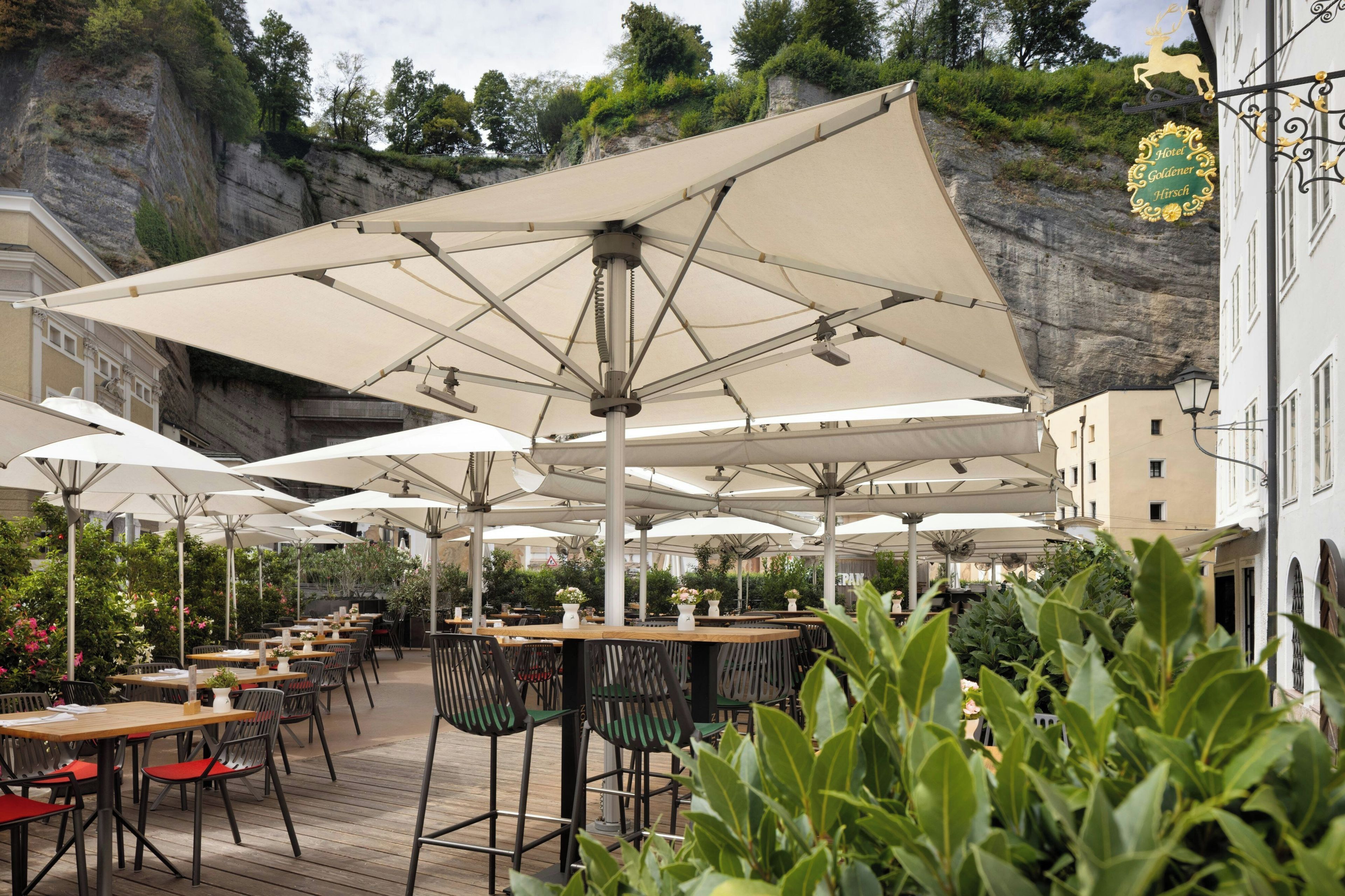 An outdoor seating area with tables and chairs under large umbrellas, overlooking a rocky cliff.