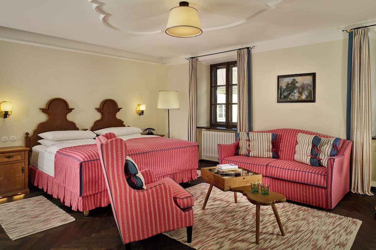 A bedroom with a double bed, a red-striped sofa, a wooden coffee table, and a nightstand with a lamp.