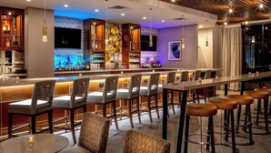 A bar area with wooden bar counters, bar stools, and a long table with chairs. - Sheraton Music City Nashville Airport (Nashville)
