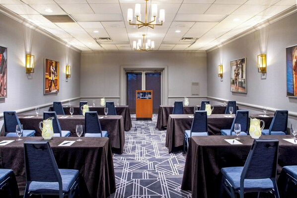 A conference room with tables set for a meeting, featuring a patterned carpet, dark tablecloths, and blue chairs.