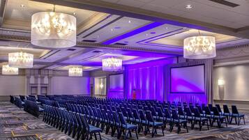 A conference room with rows of chairs, a large screen, and chandeliers.