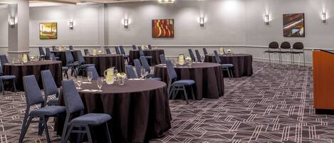 A conference room with round tables, chairs, and a carpeted floor.