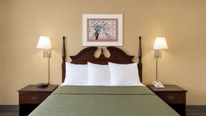 A hotel room with a large bed, two bedside tables, a nightstand, a framed artwork, and two wall-mounted lamps. - Lincoln Way Inn (Chambersburg)