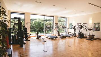 Une salle de sport spacieuse, dotée de divers appareils d’exercice, de grandes fenêtres et d’un plancher en bois.