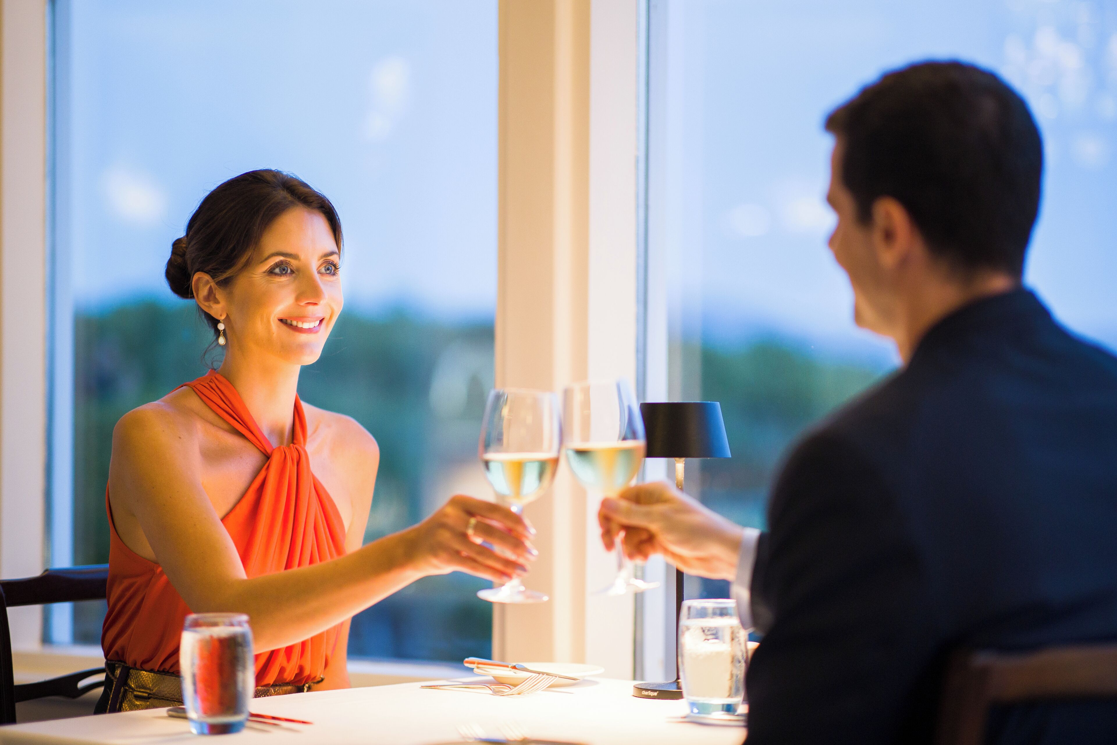 Une table à manger avec deux personnes qui trinquent avec des coupes de champagne, une bouteille d’eau et un verre d’eau.