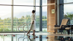 A person walking in a modern indoor pool area with large windows, a glass floor, and a view of greenery and mountains. - Parknasilla Resort and Spa (Sneem)