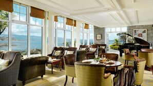 A spacious lounge with leather armchairs, a piano, and a view of the sea. - Parknasilla Resort and Spa (Sneem)
