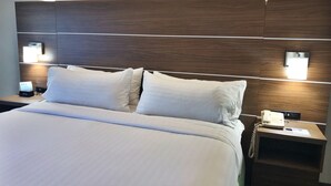 A hotel room with a large bed, two bedside tables, a nightstand, a wall-mounted TV, and a wall-mounted lamp. - Holiday Inn Express Boca Raton-West by IHG (Boca Raton)
