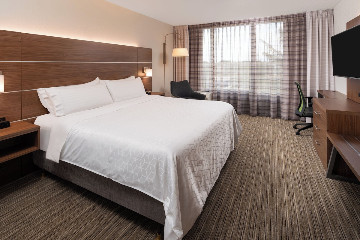 Een hotelkamer met een groot bed, nachtkastjes, een bureau, een stoel, een televisie en een raam met gordijnen.