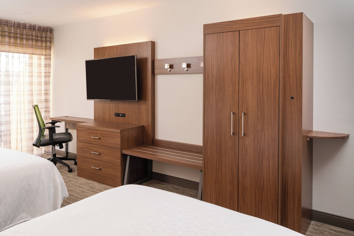 Een hotelkamer met een bed, een bureau met stoel, een wandtelevisie en een kledingkast.