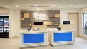 A hotel reception desk with a digital display, a Holiday Inn Express sign, and a vending machine in the background.