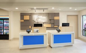 A hotel reception desk with a digital display, a Holiday Inn Express sign, and a vending machine in the background.