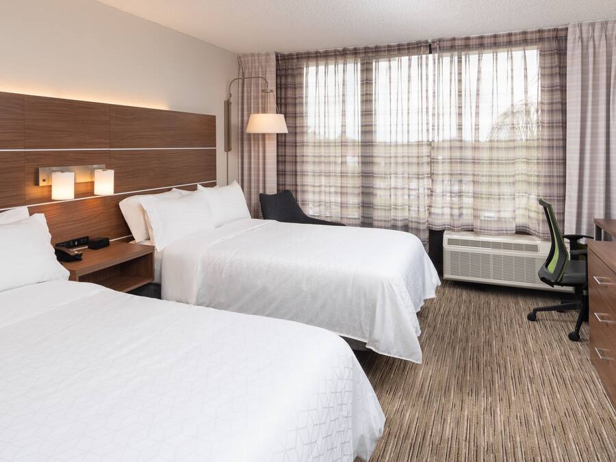 A hotel room with two beds, a desk, a chair, a TV, and a window with curtains.
