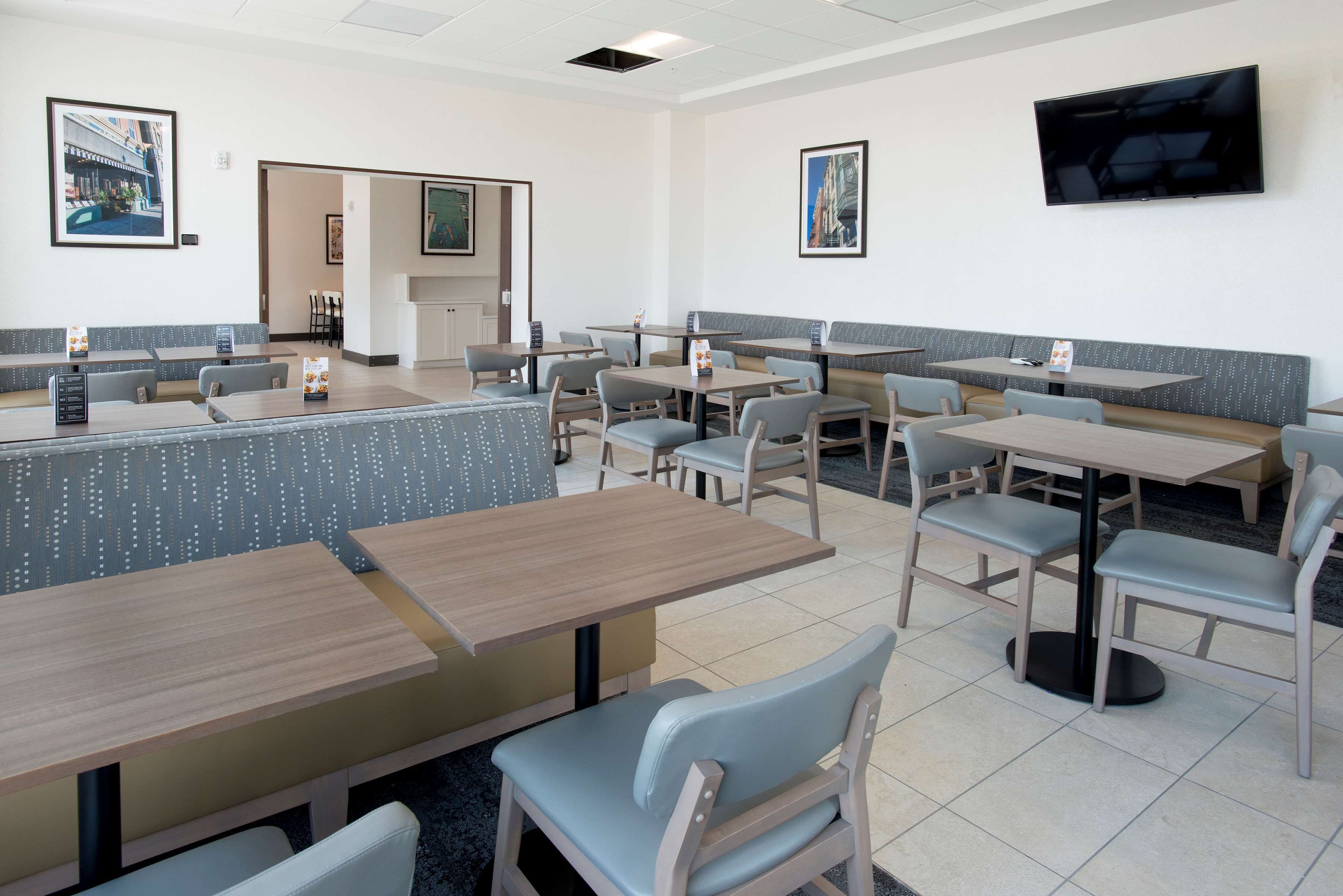 A clean, modern dining area with multiple tables and booths, a flat-screen TV mounted on the wall, and framed artwork on the walls.