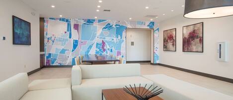 A modern hotel lobby with a large map mural, a seating area, and a wooden table with a decorative centerpiece.