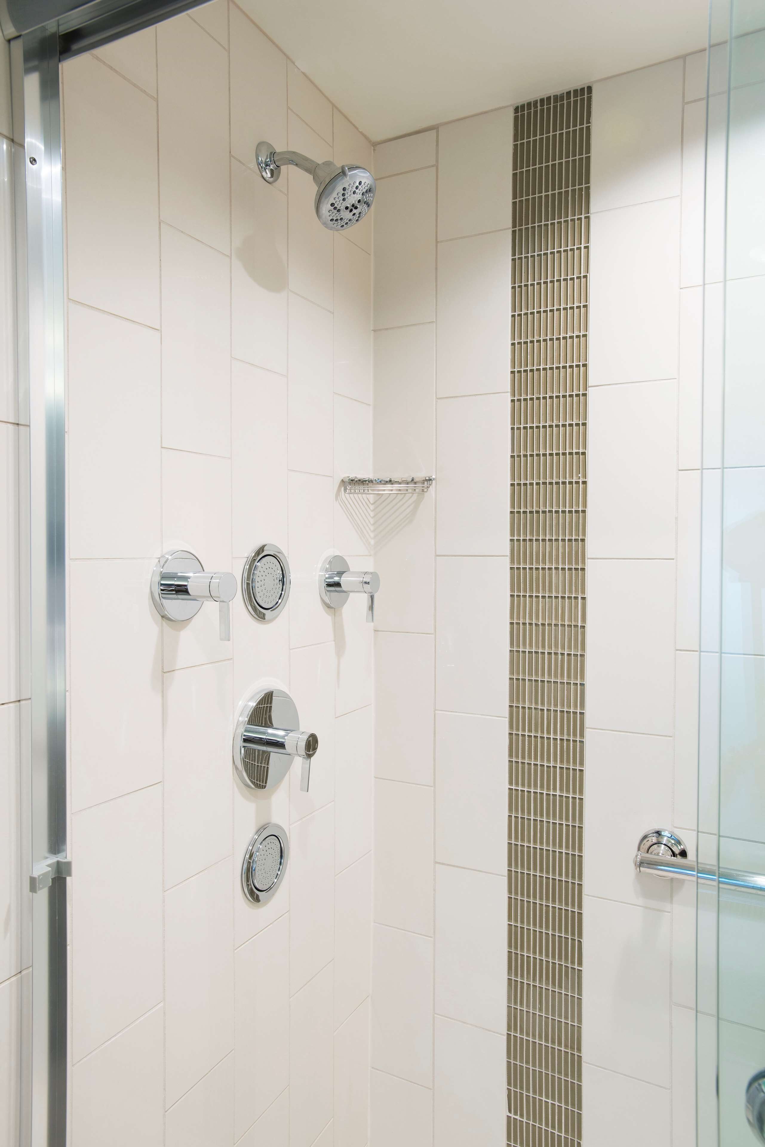 A modern bathroom with white tiled walls, a glass shower enclosure, and a vertical mosaic tile accent.