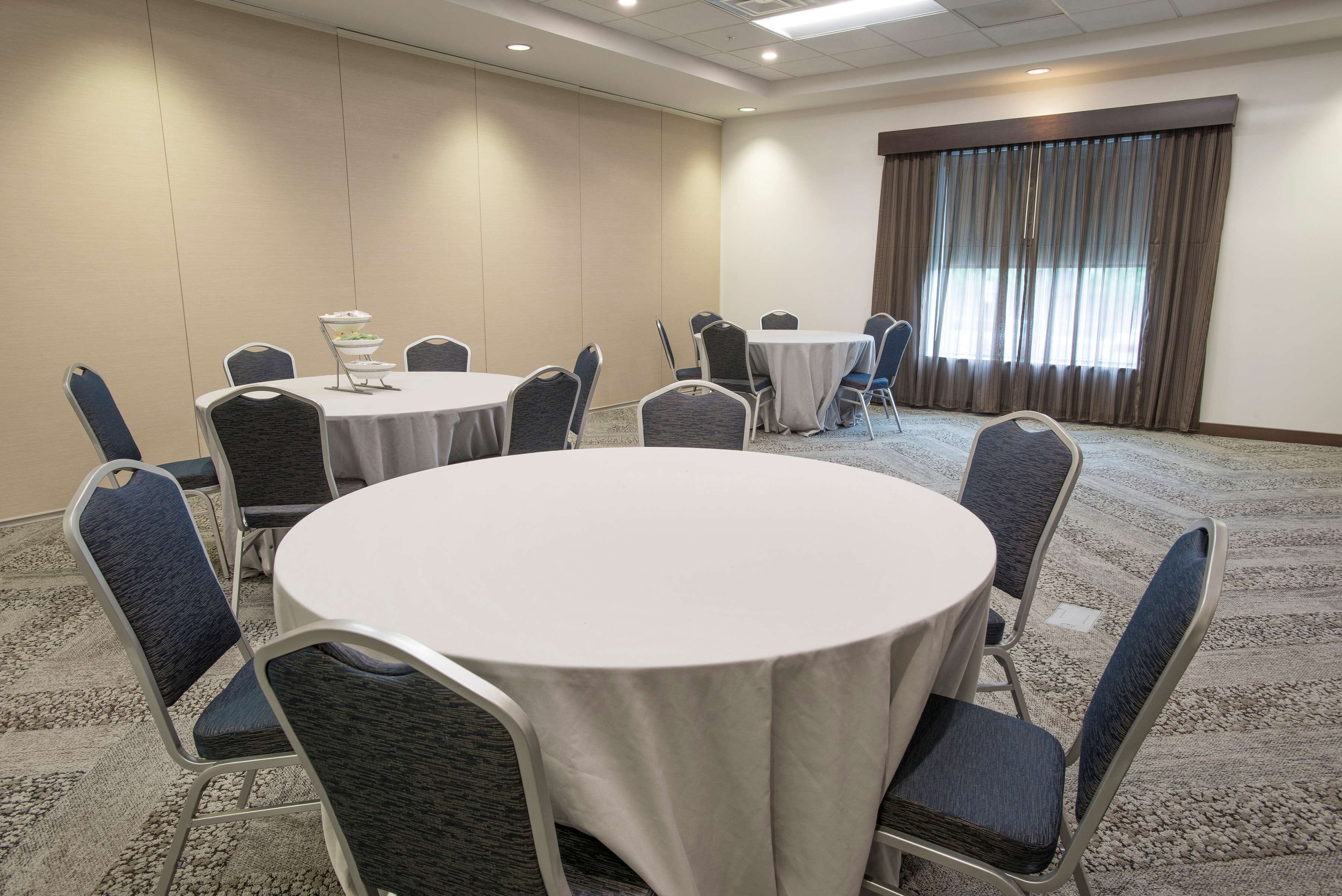 A conference room with round tables and chairs, a carpeted floor, and a large window with curtains.
