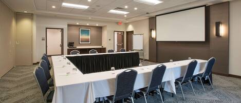 A conference room with a long table, chairs, a projector screen, and a whiteboard.