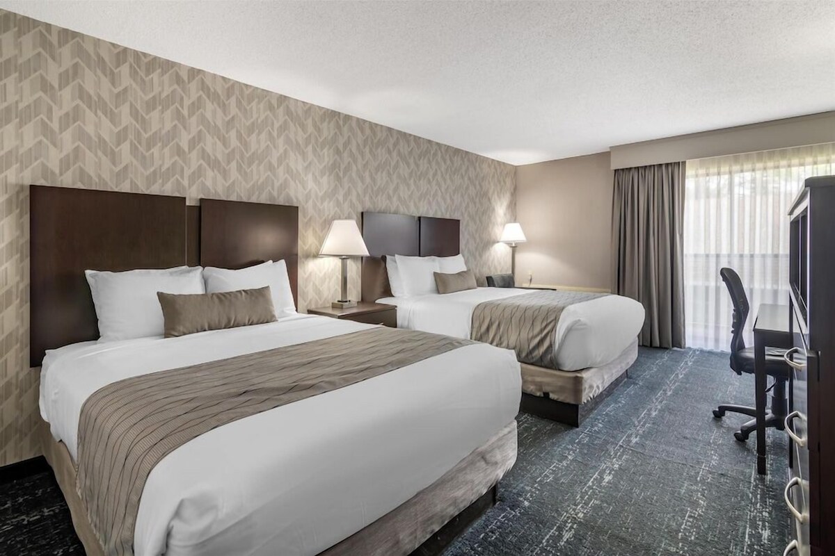 A hotel room with two beds, a desk, a chair, and a television.