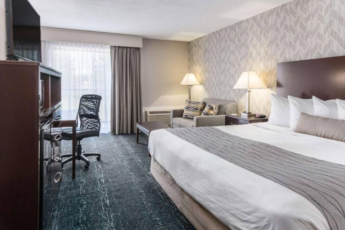 A hotel room with a bed, desk, chair, and two lamps.