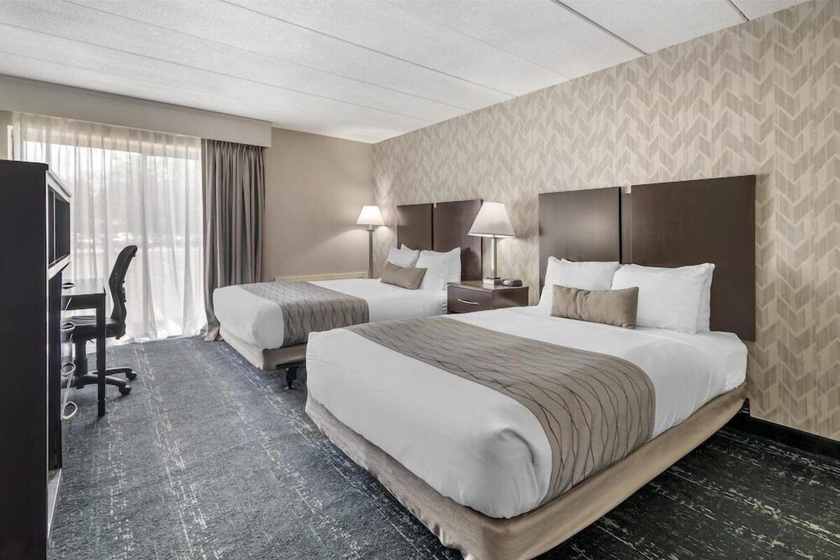 A hotel room with two beds, a desk, a chair, and a television.